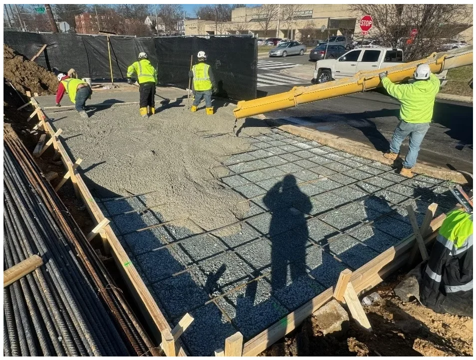 Crawford Gardens — site concrete pour underway with finishing crew shaping a reinforced pad at street level.